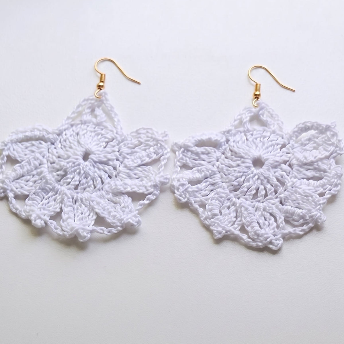 Par de pendientes de crochet blancos con forma de abanico calado y enganche metálico abierto sobre fondo claro.