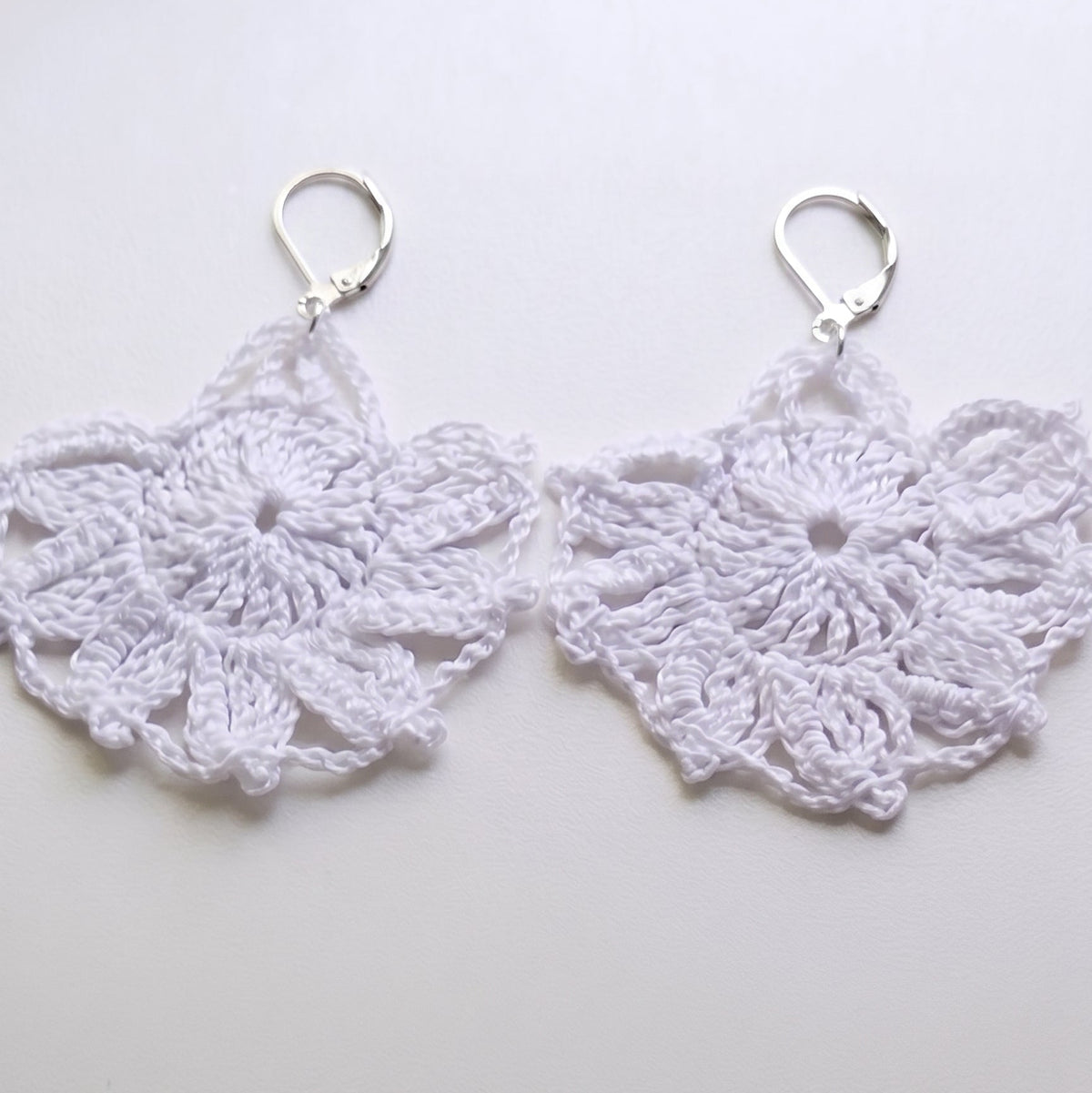 Par de pendientes de crochet blancos con forma de abanico calado y enganche metálico tipo ballestilla sobre fondo claro.