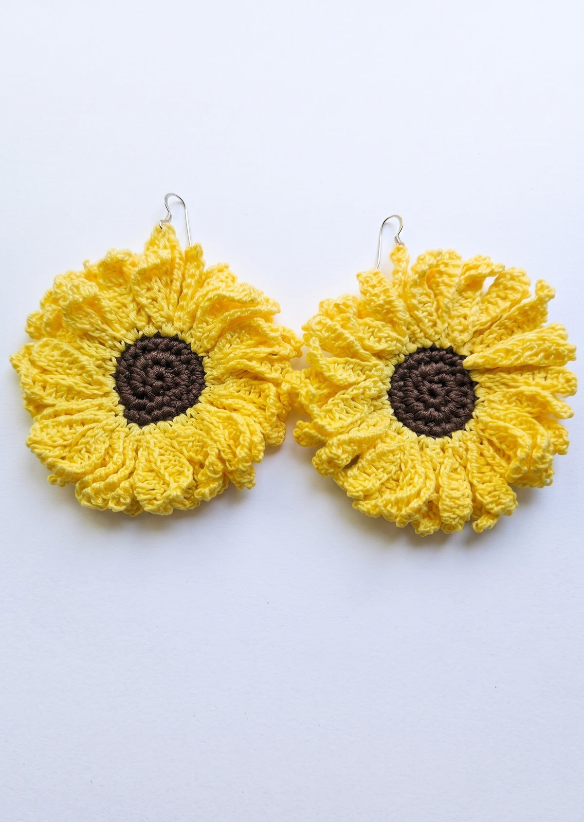 Par de pendientes de crochet con forma de girasol con hojas amarillas y centro marrón.